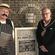 Cllr Nic Hodges, dressed as a Victorian Butcher, with Mayor of Barry, Cllr Steffan Wiliam. The poster shows the front of Mrs Wilson’s Temperance Bar on Barry’s Holton Road, where non-alcoholic drinks were sold